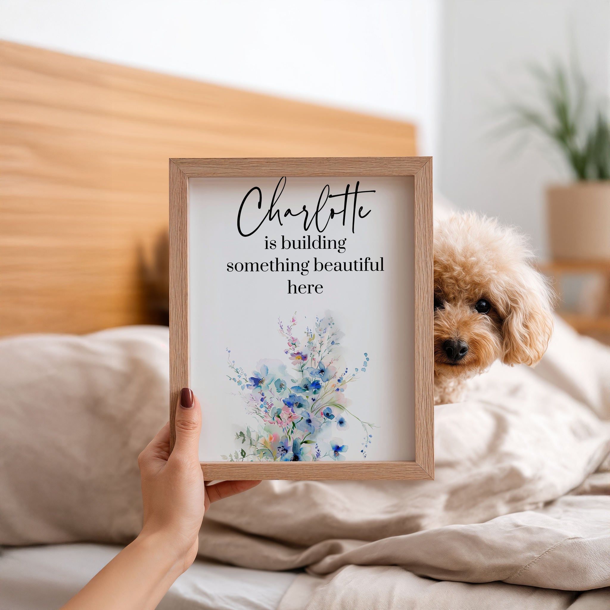 Woman holding a small framed print with a dog peeking from behind the right side.