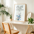 Framed artwork on a table with plants and a chair in a bright room