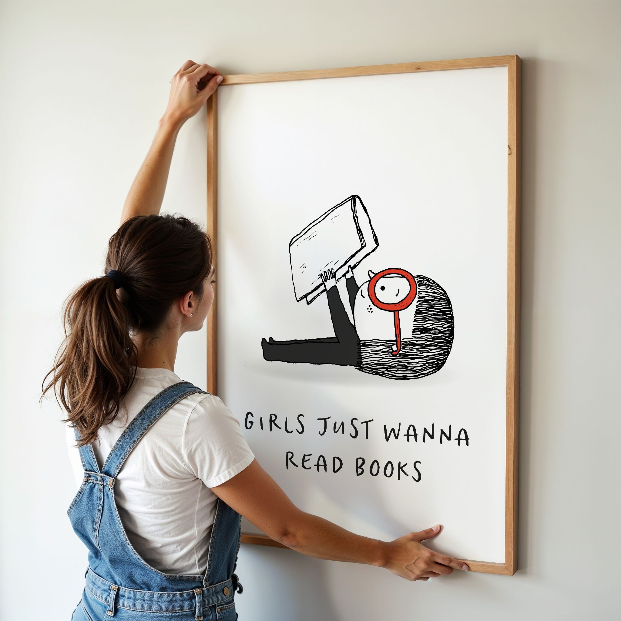 Woman in overalls hanging a framed illustration with text 'Girls just wanna read books' on a wall