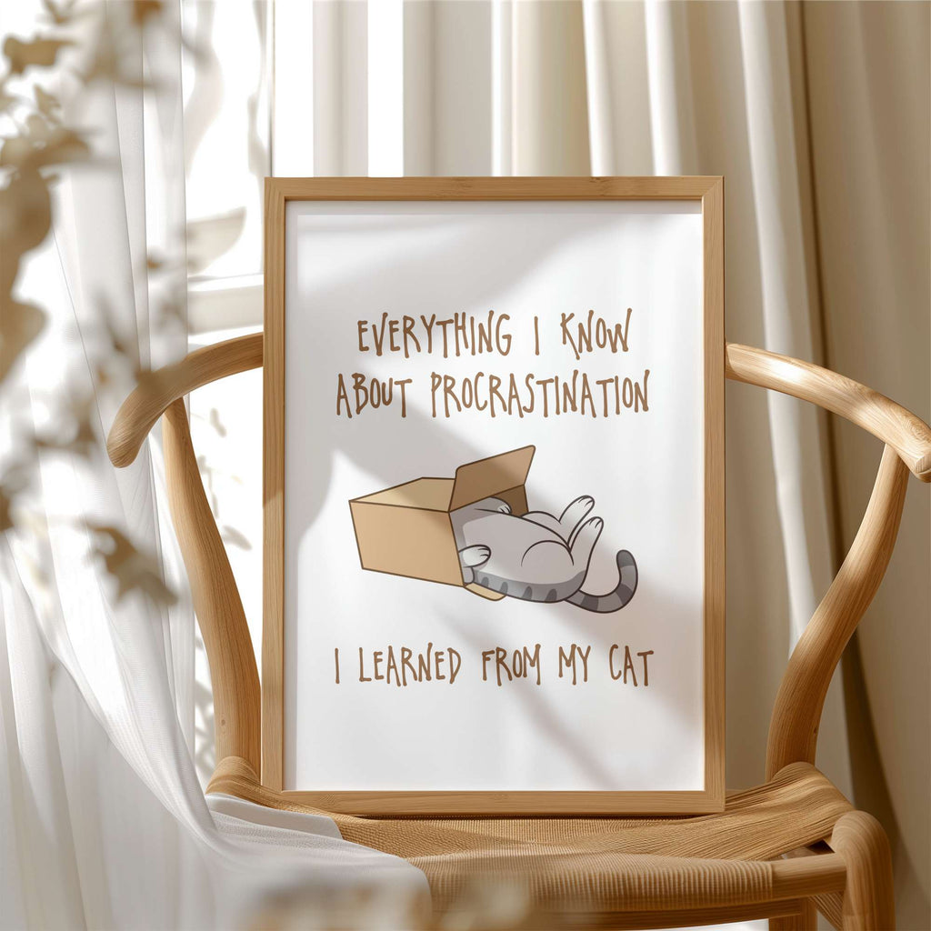 Framed print with a cat illustration and text about procrastination, on a wooden chair.
