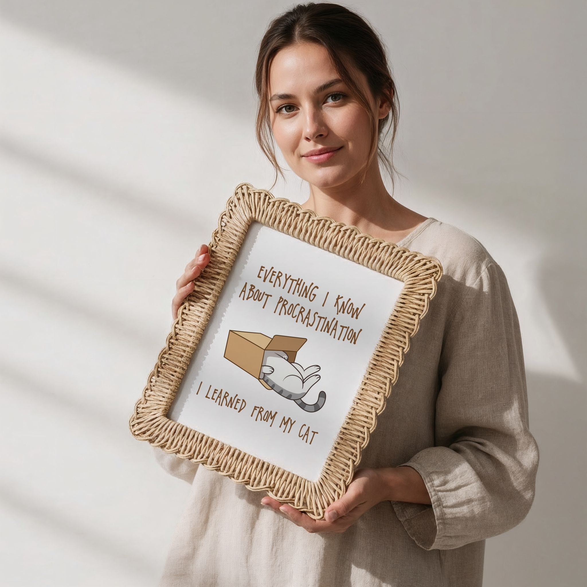 Woman holding a framed picture with text and a whimsical cat illustration on a plain background