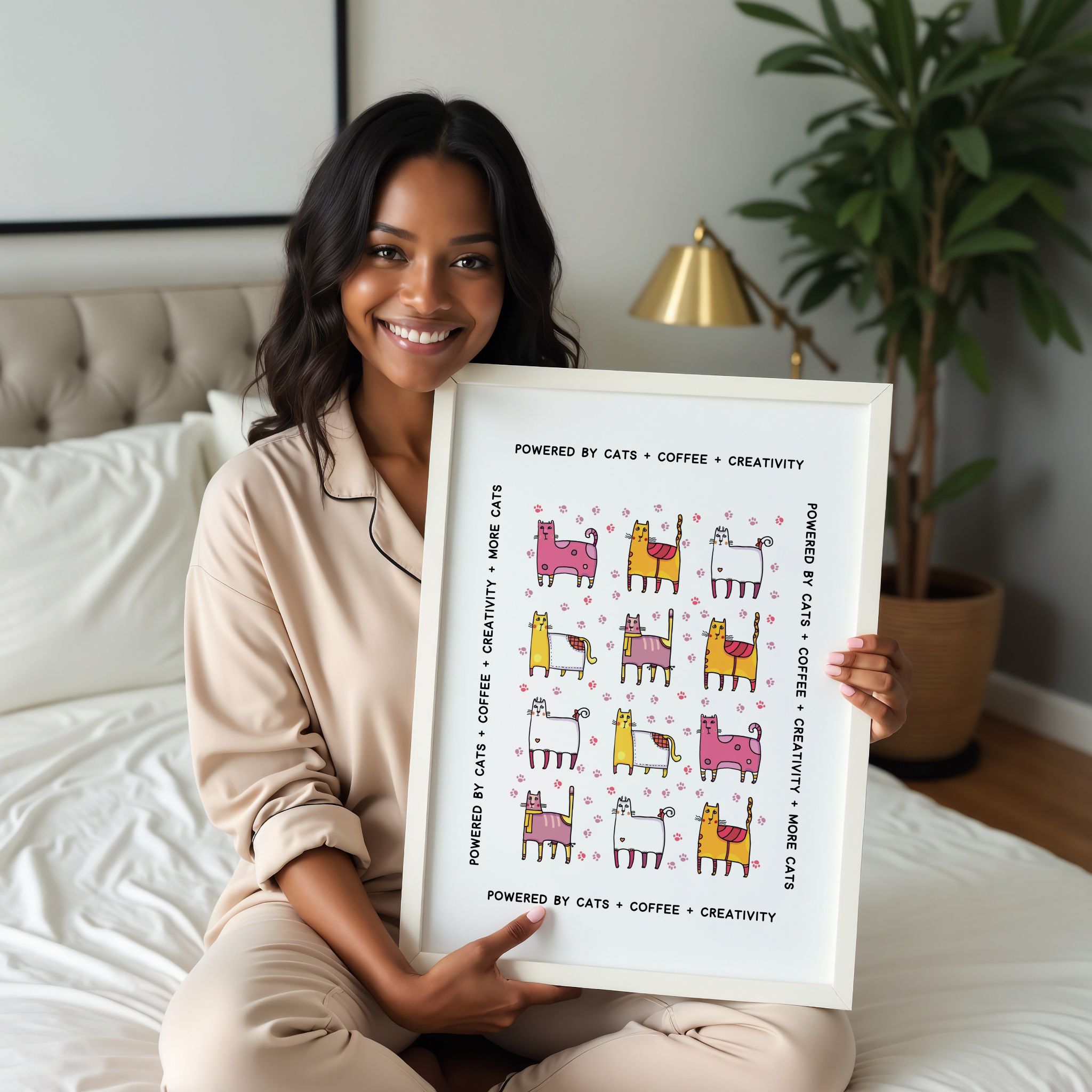 Woman holding a framed print with colorful illustrations of cats and text in a bedroom setting.