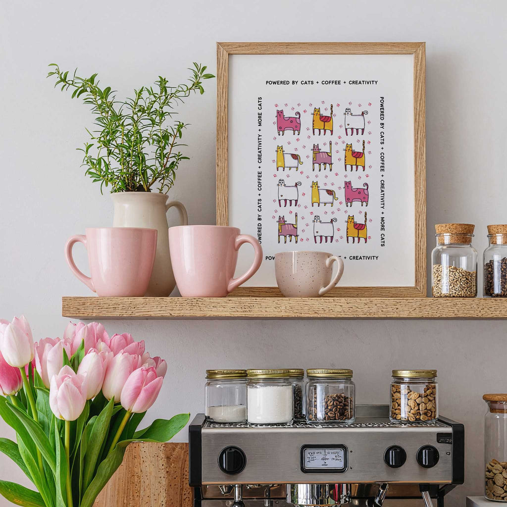 Shelf with pink mugs, a plant, a framed whimsical cats + coffee print, and jars above a coffee machine