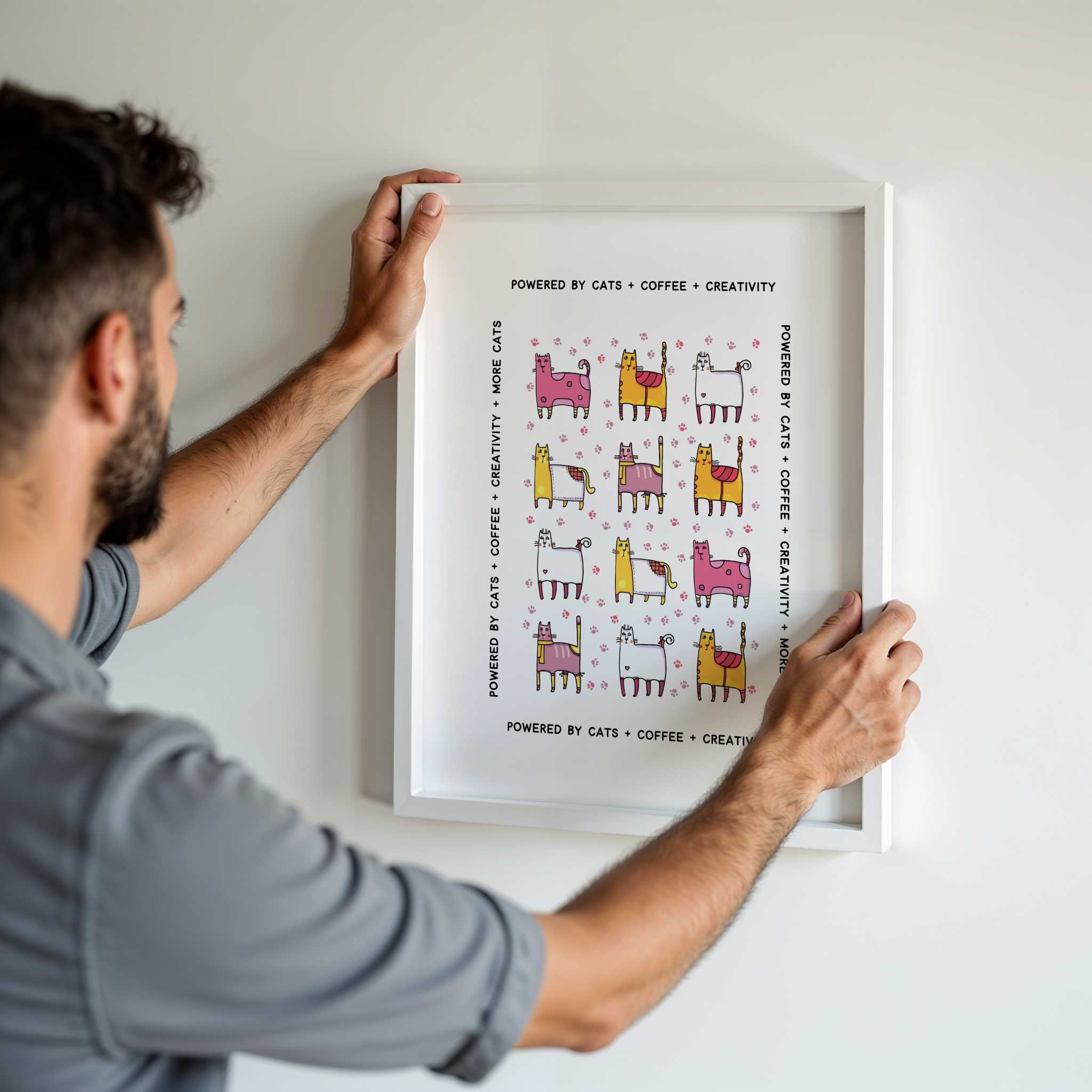 Man hanging a framed print of colorful whimsical cats on a white wall.