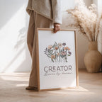 Woman holding a framed print with floral design and text 'Creator Driven by dreams' in a home setting