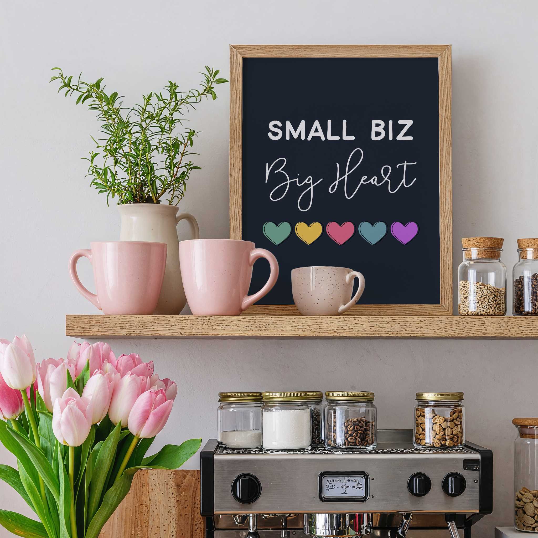 Kitchen shelf with mugs, a plant, and a framed print reading 'Small Biz Big Heart' on a light gray wall.