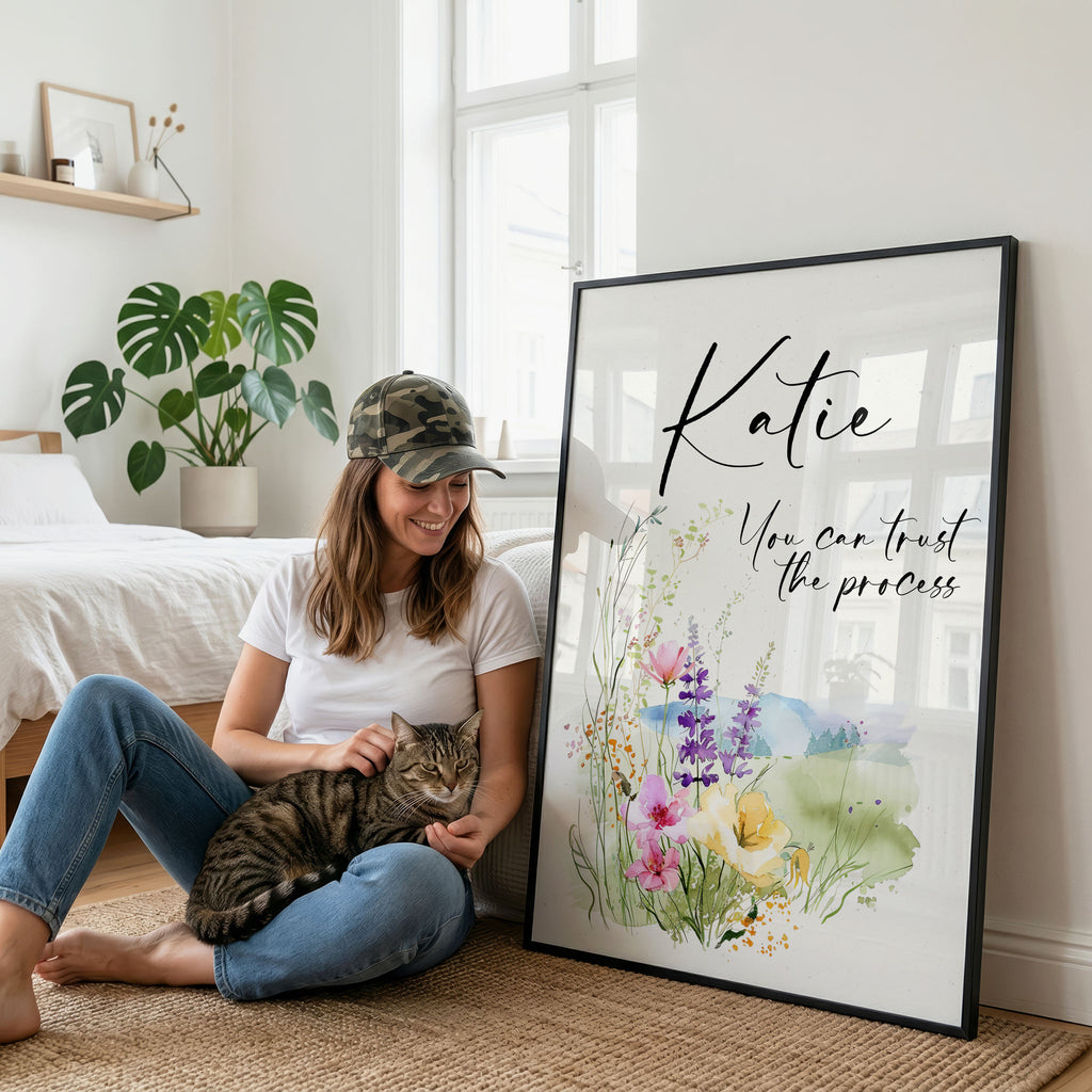 Woman holding a cat, smiling at a large framed print with flowing text and watercolor flowers