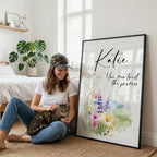 Woman holding a cat, smiling at a large framed print with flowing text and watercolor flowers